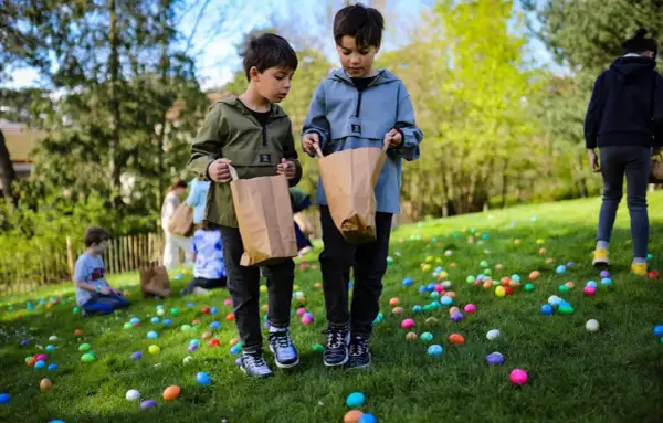 Deux enfants cherchent des œufs colorés dans l'herbe lors d'une chasse aux œufs à Paris.