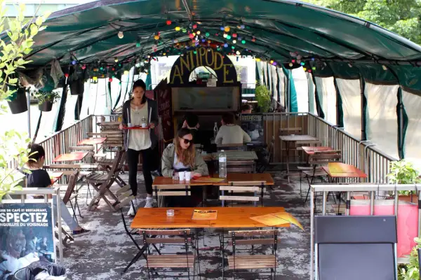 Terrasse animée d'un café-restaurant sur une péniche à Paris, avec des tables en bois, des lumières colorées et des plantes.