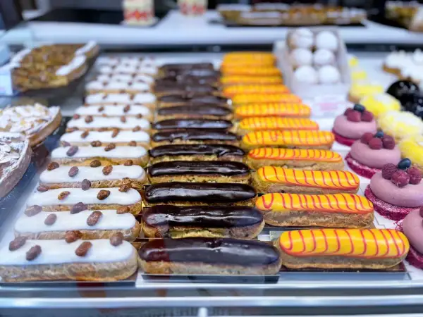 Une alléchante liste pâtisserie française : éclairs au chocolat, à la vanille et au glaçage jaune rayé de rouge, ainsi que des tartelettes aux amandes.