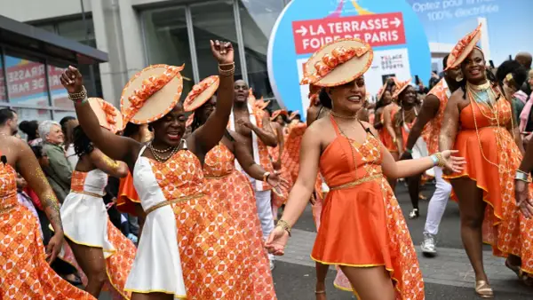 Des danseuses en tenues orange et blanches, chapeaux assortis, célèbrent la foire de Paris 2026 dans une ambiance festive.