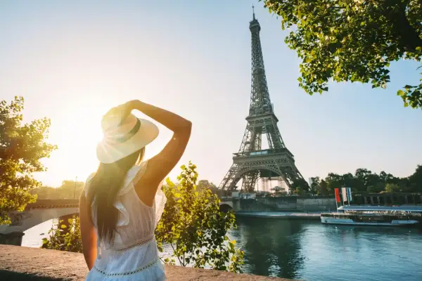 Une femme au chapeau admire la Tour Eiffel au coucher du soleil, profitant des activités parisiennes.