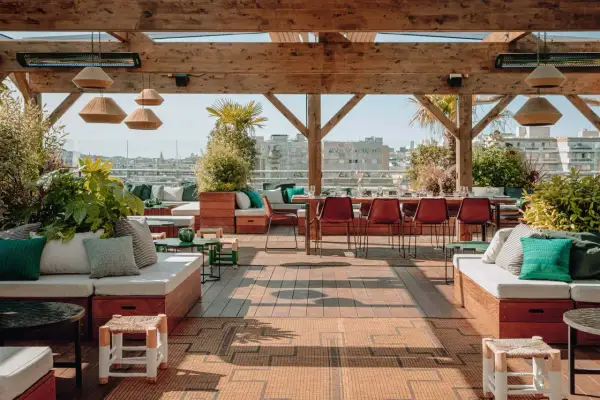 Le perchoir Ménilmontant, un rooftop chic avec vue sur Paris. Canapés confortables, tables dressées, végétation luxuriante et ambiance estivale.