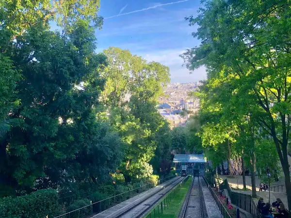 Vue sur le funiculaire de Montmartre, avec Paris en arrière-plan. Les arbres verdoyants encadrent la scène.