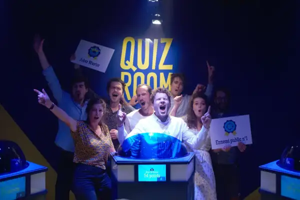 Équipe joyeuse dans une "Quiz Room" à Paris La Villette, célébrant une victoire. Ils tiennent des pancartes "Joker Master" et "Ennemi public n°1".