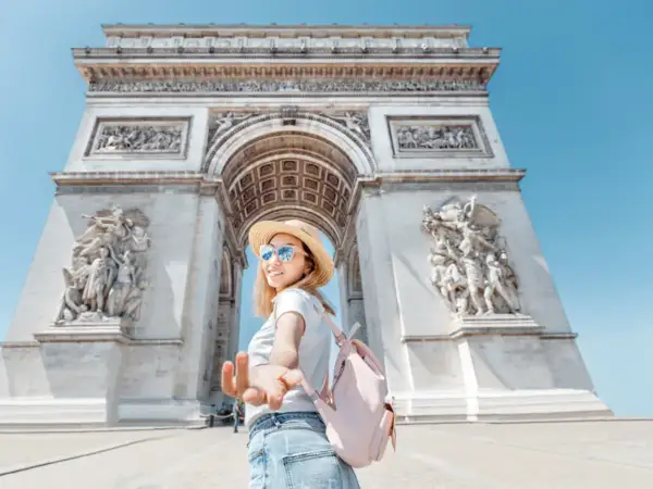 Une jeune femme tend la main devant l'Arc de Triomphe. L'accès au monument est gratuit, une belle opportunité de visite.