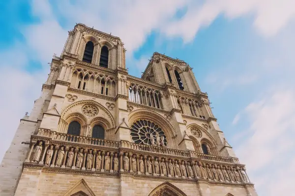 Notre Dame de Paris, une visite inoubliable. La façade majestueuse de la cathédrale se dresse sous un ciel bleu et nuageux.