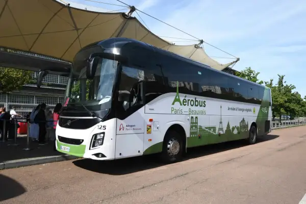L'Aérobus Paris-Beauvais, un bus blanc et vert orné de monuments parisiens, attend des passagers sous une structure de toit.