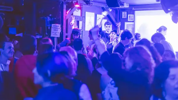 Ambiance festive dans un bar du Marais, une foule profite de la musique sous des lumières bleues et violettes.