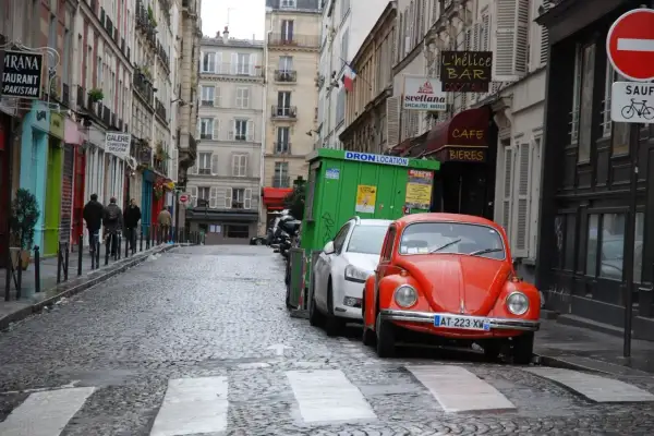 Une rue pavée à Paris, avec une Coccinelle rouge garée. Un panneau "parking gratuit Paris" serait le bienvenu ici.