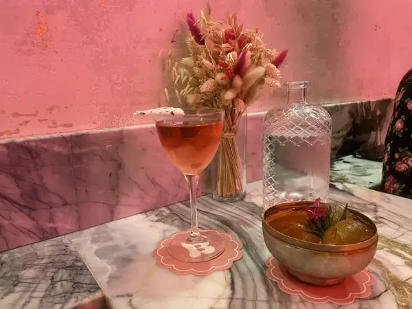 Un cocktail rose et un bol de fruits sur un marbre rose, ambiance douce et romantique d'un bisou bar.