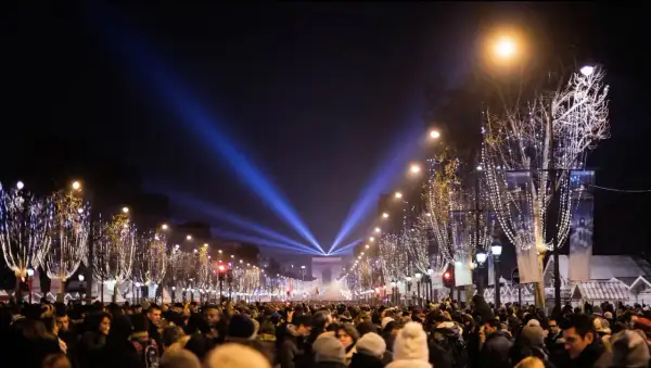 Une foule nombreuse célèbre une **soirée paris** sous les lumières bleues illuminant l'Arc de Triomphe et les arbres décorés de guirlandes.