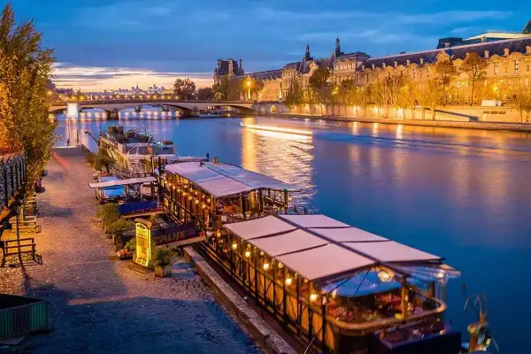 Un restaurant sur Seine à Paris, illuminé et accueillant, reflète ses lumières sur l'eau paisible.