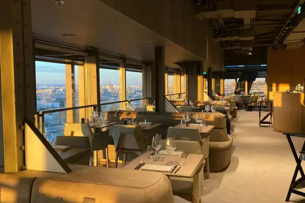 Intérieur d'une brasserie chic avec vue panoramique sur Paris. Les tables sont dressées, prêtes à accueillir les clients pour un dîner inoubliable à la Madame Brasserie Tour Eiffel.