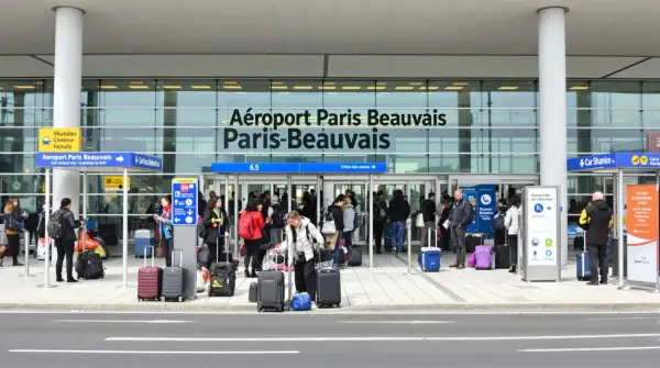 Voyageurs avec bagages devant l'aéroport Paris-Beauvais, prêts pour leur vol.
