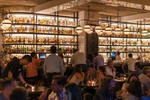 Ambiance chaleureuse dans ce bar gay, avec des étagères remplies de bouteilles et des clients attablés.