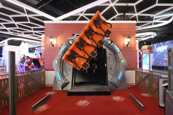 Attraction de manège orange suspendue, prête à faire décoller les visiteurs. Le sol rouge est décoré de motifs "La tête dans les nuages".