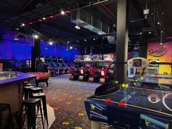 Ambiance de fête foraine à Montparnasse, avec des jeux d'arcade, des tables de air hockey et des murs décorés "Smile world".