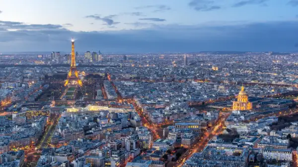Vue panoramique de Paris au crépuscule, avec la Tour Eiffel illuminée et le dôme des Invalides. On aperçoit le quartier de La Défense au loin. Un panorama depuis l'**étage tour Montparnasse**.
